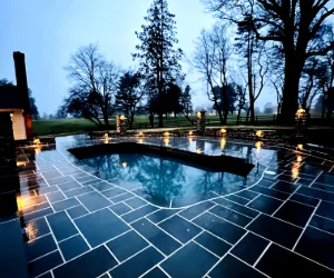 Black stone tiles with white grout surrounding a pool